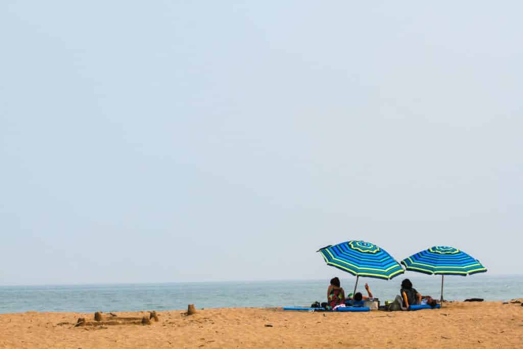 Two people under beach umbrellas during middle of the day