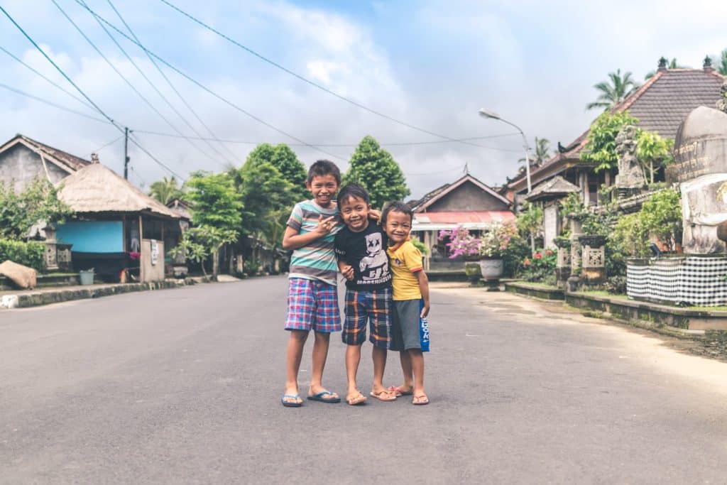 Three smiling kids standing on the street.