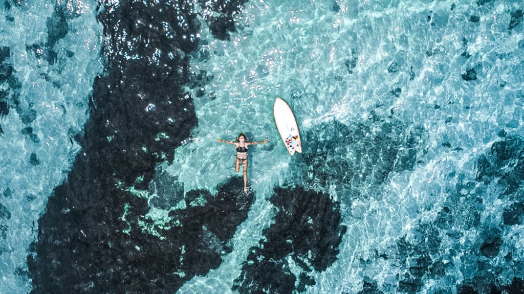 An image of a person floating and posing in the ocean with surfboard floating next to them