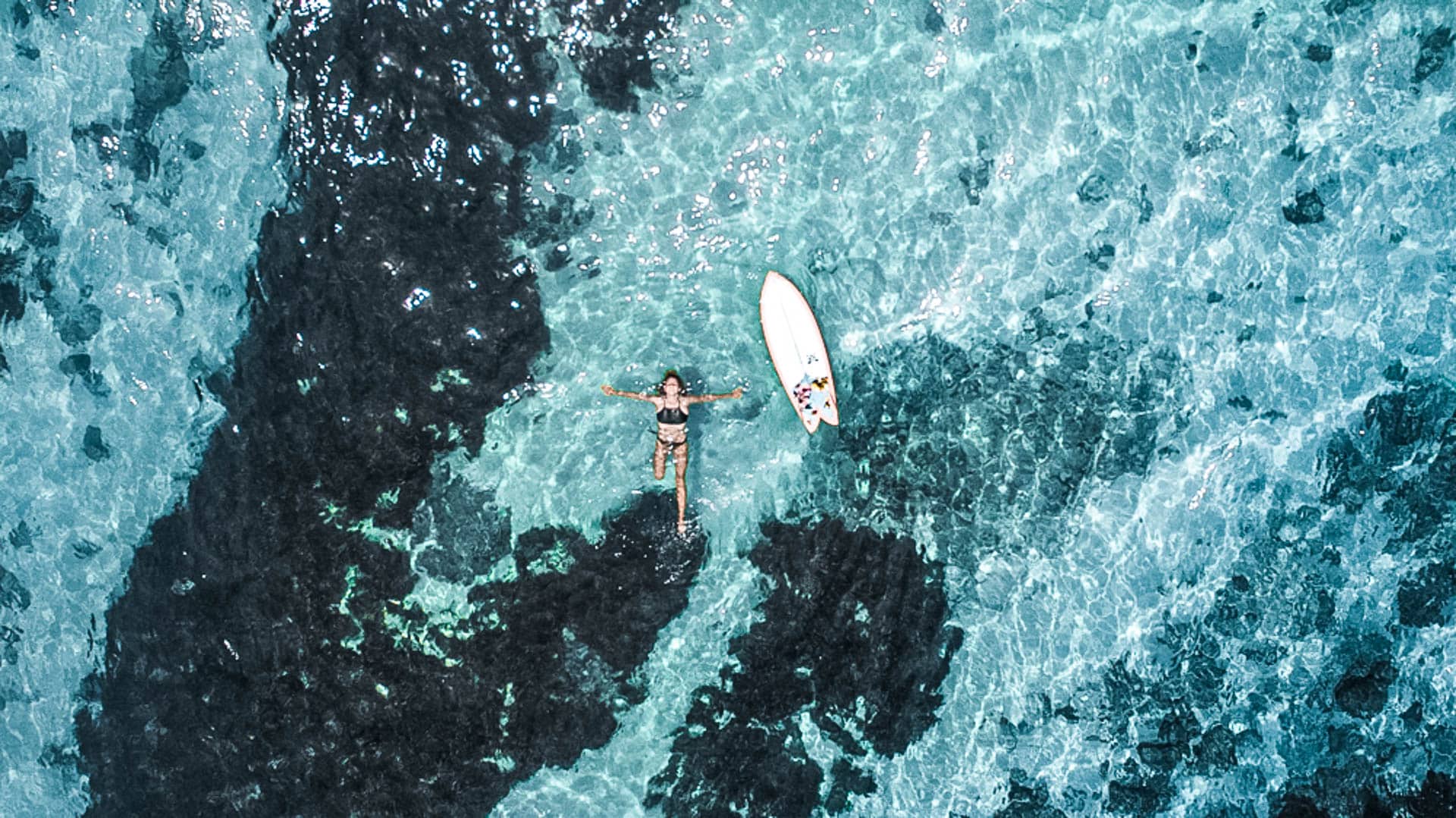 An image of a person floating and posing in the ocean with surfboard floating next to them