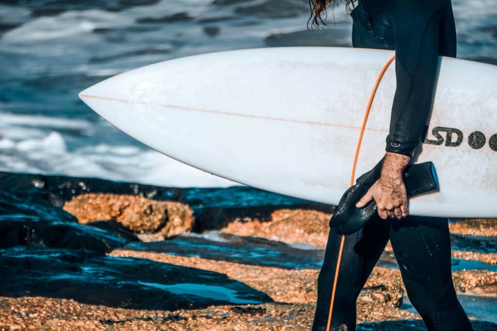 A person in wetsuit walking with a surfboard in hand.