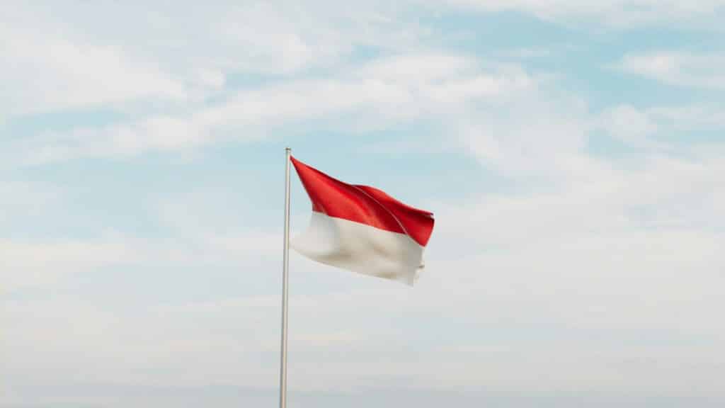 An image of the Indonesian flag blowing in the wind with a cloudy sky as the background