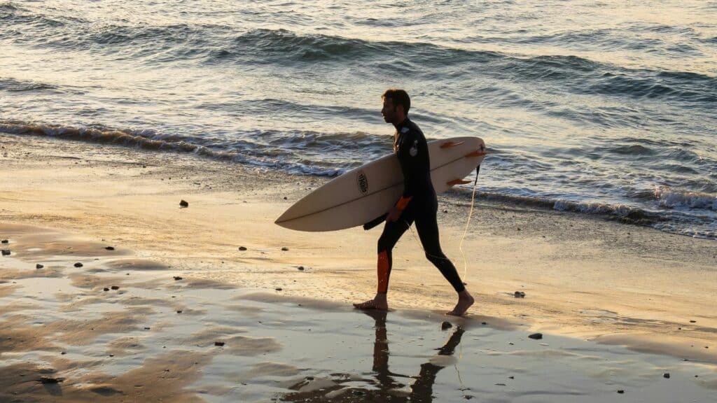 An image of a surfer holding an epoxy surfboard leaving the ocean