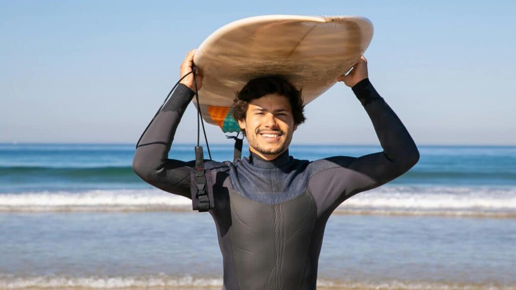 An image of a surfer wearing a wetsuit and holding a surfboard on his head