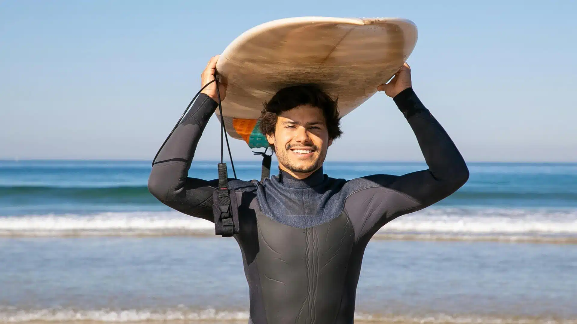 An image of a surfer wearing a wetsuit and holding a surfboard on his head