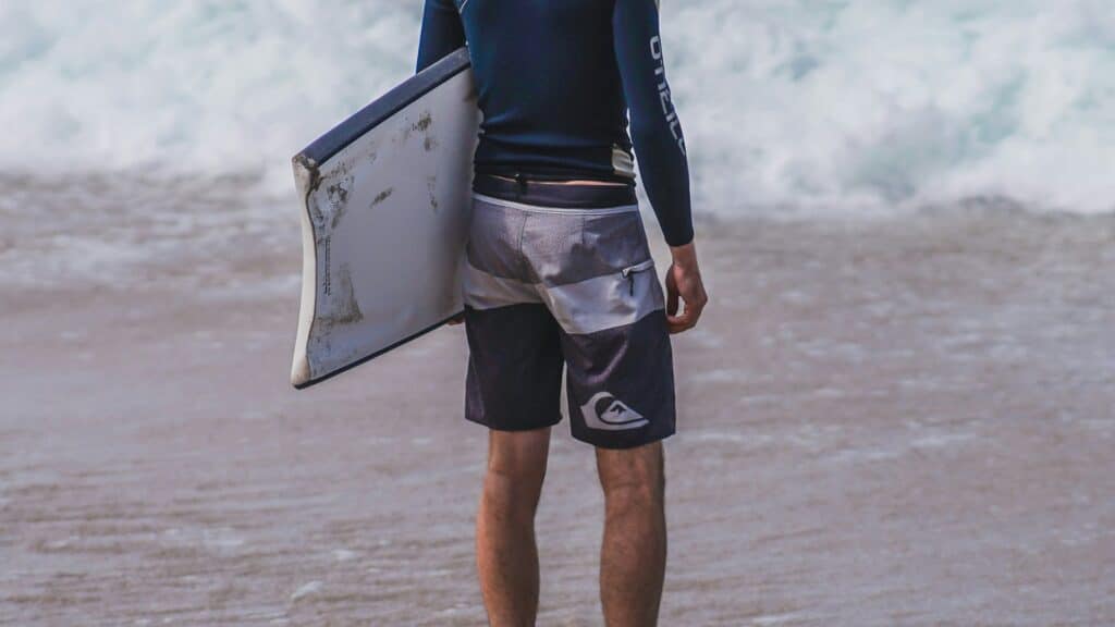An image of a man wearing board shorts, holding a short board about to enter the sea