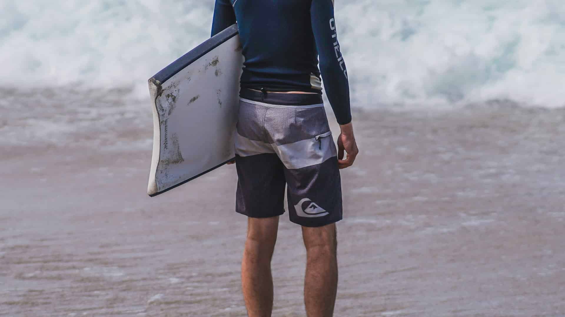 An image of a man wearing board shorts, holding a short board about to enter the sea