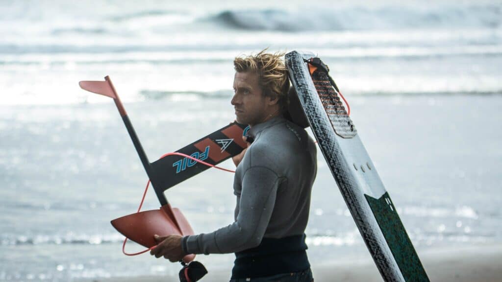 An image of a surfer in a wetsuit holding a foilboard