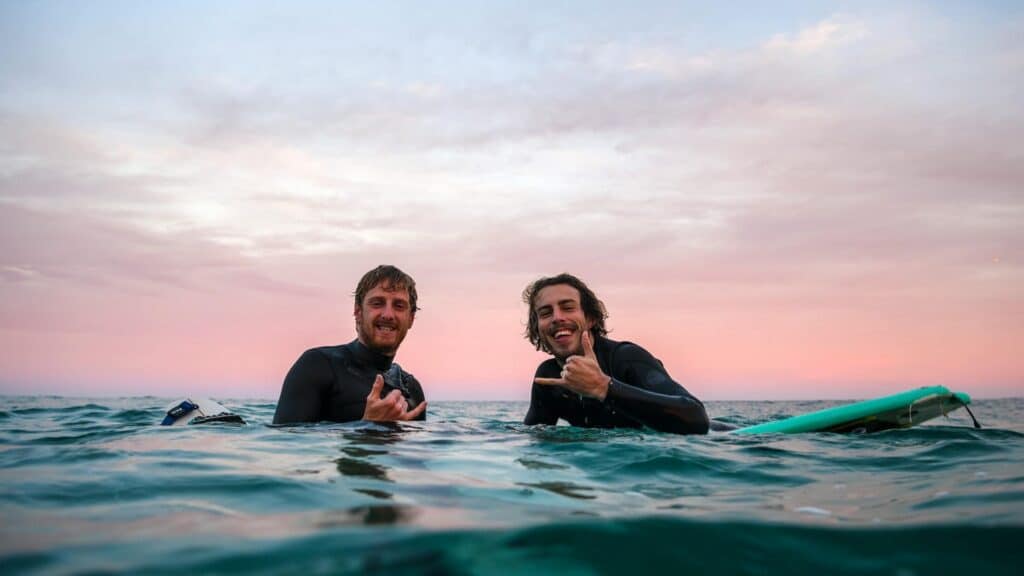 An image of two surfers in the sea showing respect and good vibes with the shaka