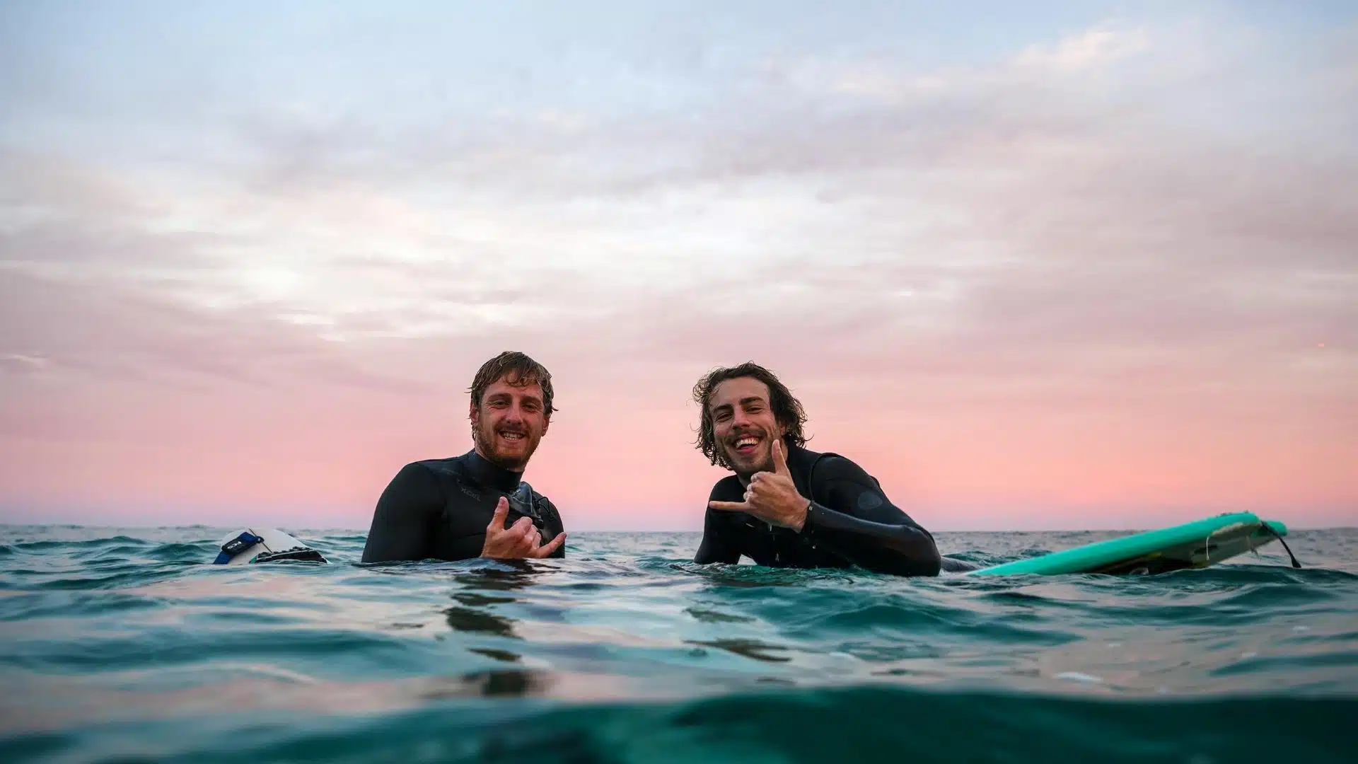 An image of two surfers in the sea showing respect and good vibes with the shaka