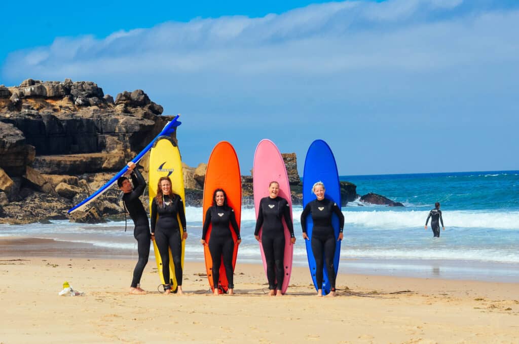 People posing on the beach with their surfboards and ocean behind them.