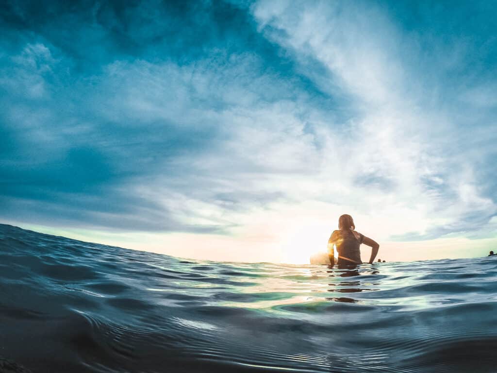 Person looking onto the sunset on a surfboard.
