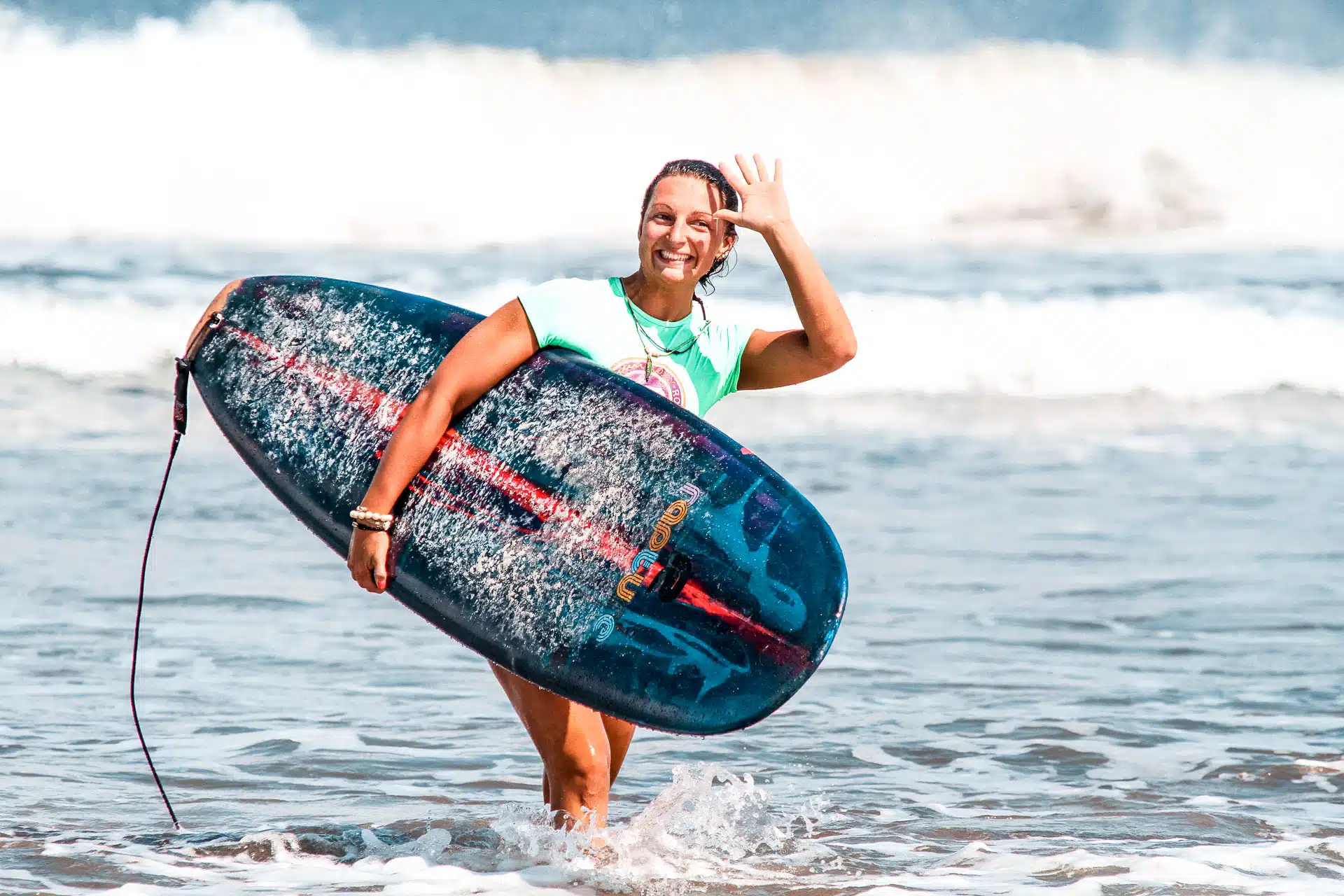 An image of a rapture surfcamp guest waving at the camera she is holding a surfboard