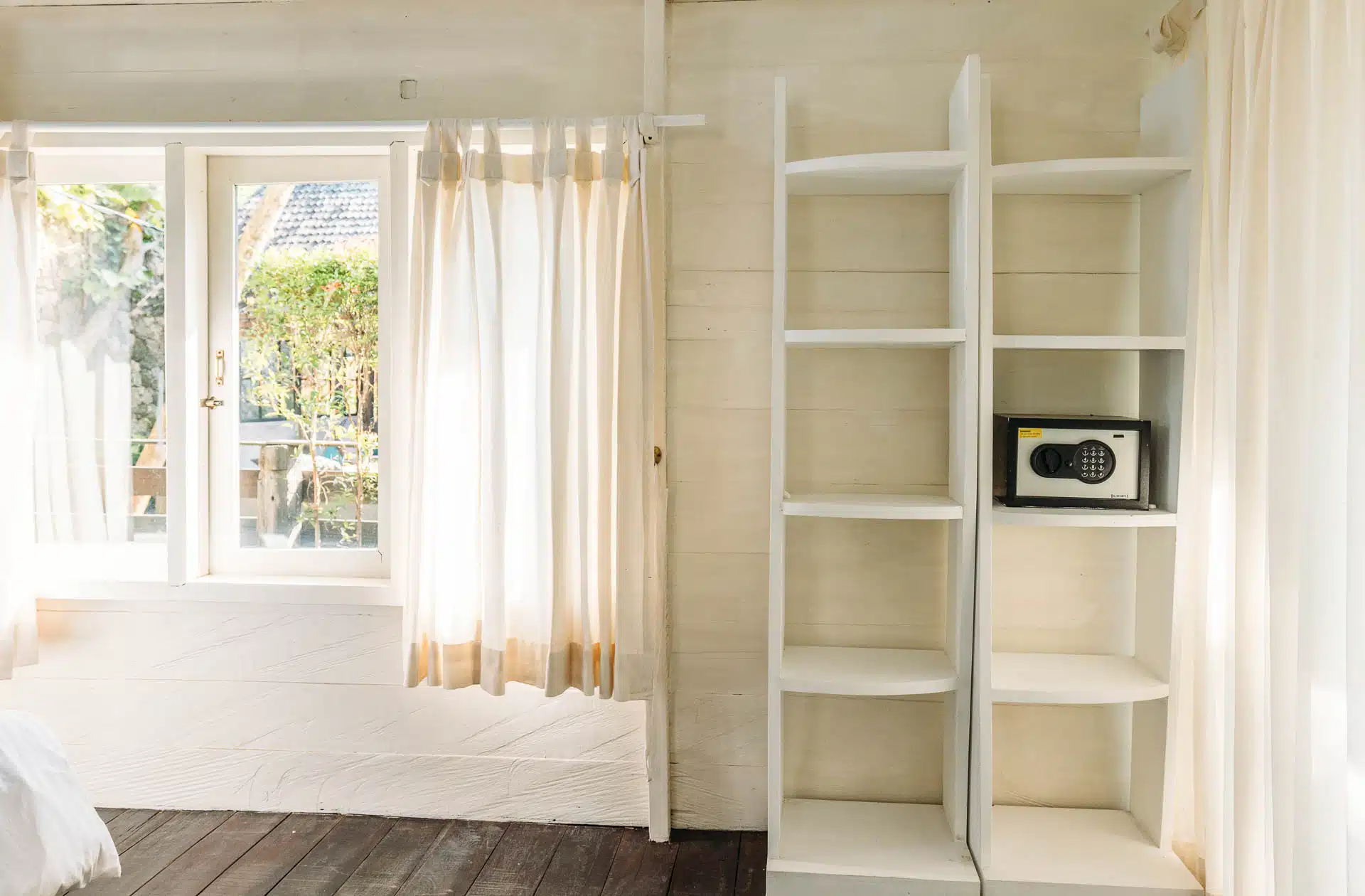 A hotel room with a wide window and pool view and shelves on the side