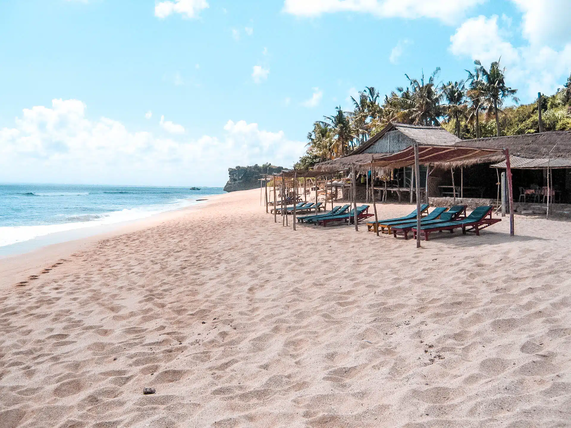 An empty white sand beach with lounge chairs lined up under canopies.