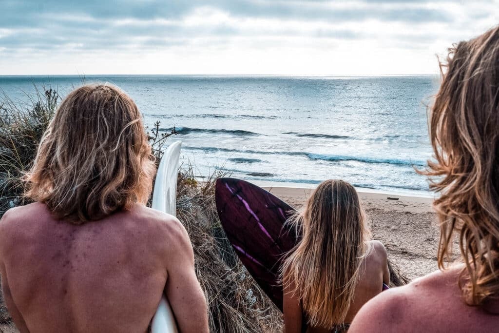 Group of people holding surfboard and looking towards the ocean with their back towards the camera
