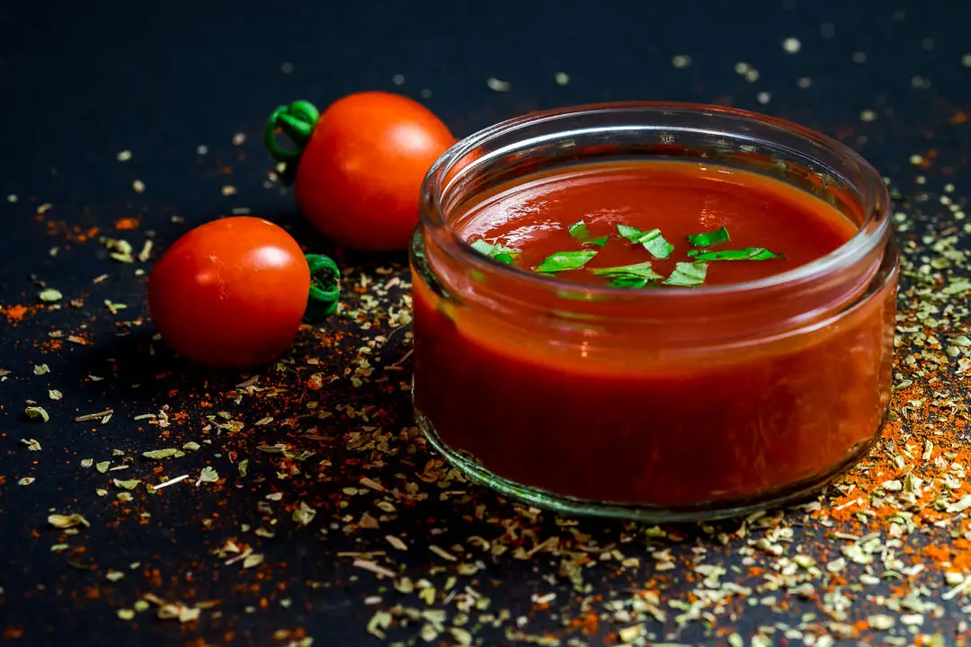 Ein Glas mit roter Ketchup-Sauce und zwei Tomaten