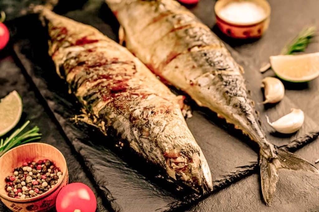 Two grilled mackerels in a black stone board