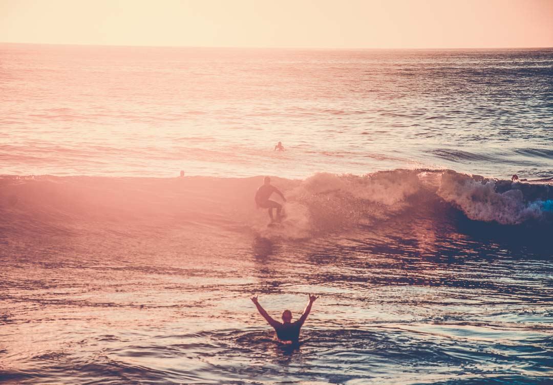 Group of surfers with wave on the sunset