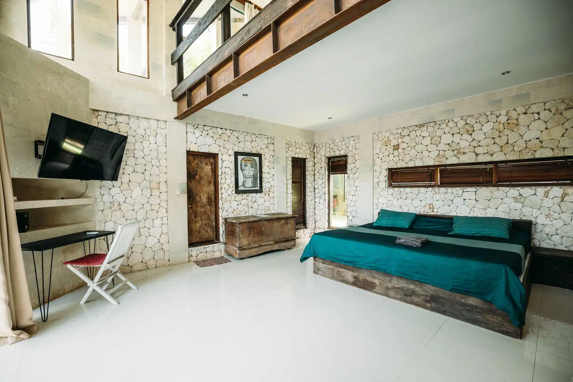 A hotel room with stone walls with a working desk and TV and a comfortable king-size bed