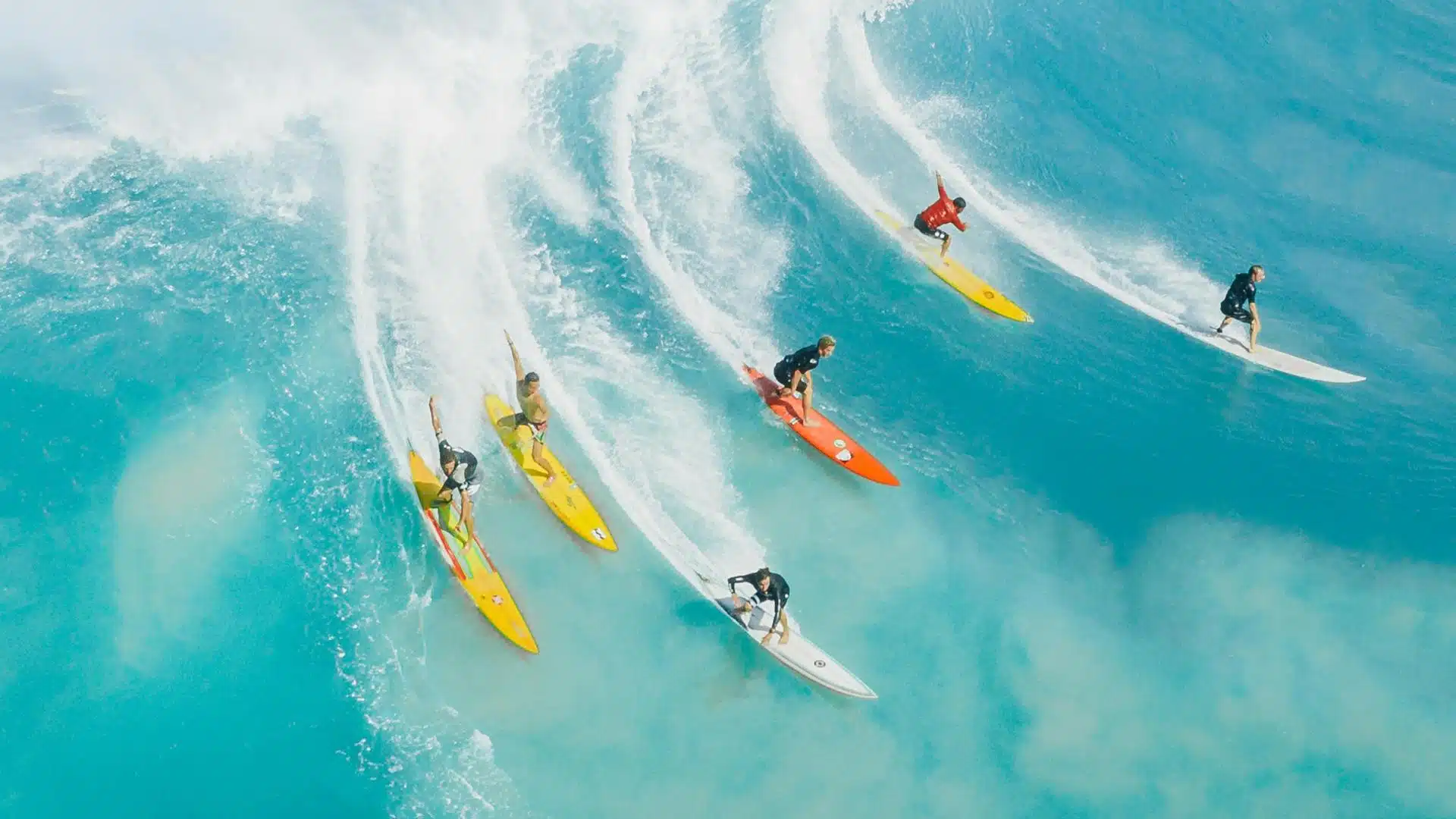 An image of six longboard surfers in the ocean they are riding a wave