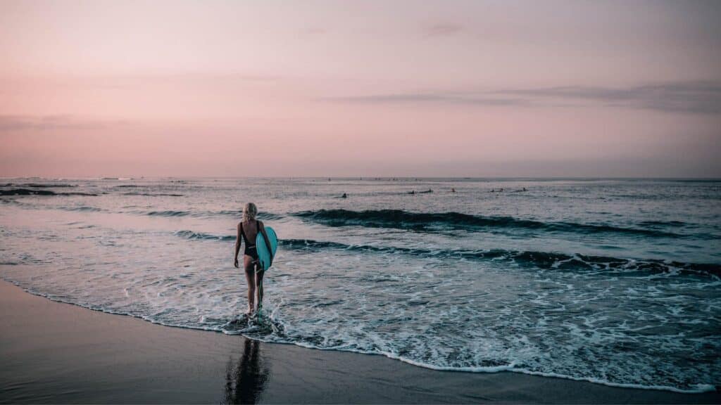 An image of a solo travelling surfer walking into the sea in portugal
