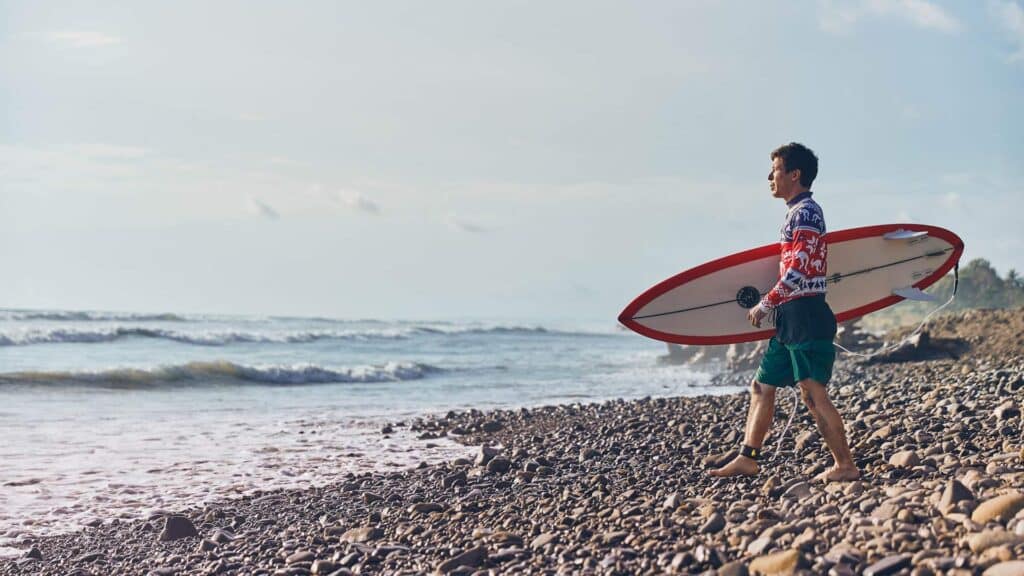 An image of a surfer stood at the beach holding a board
