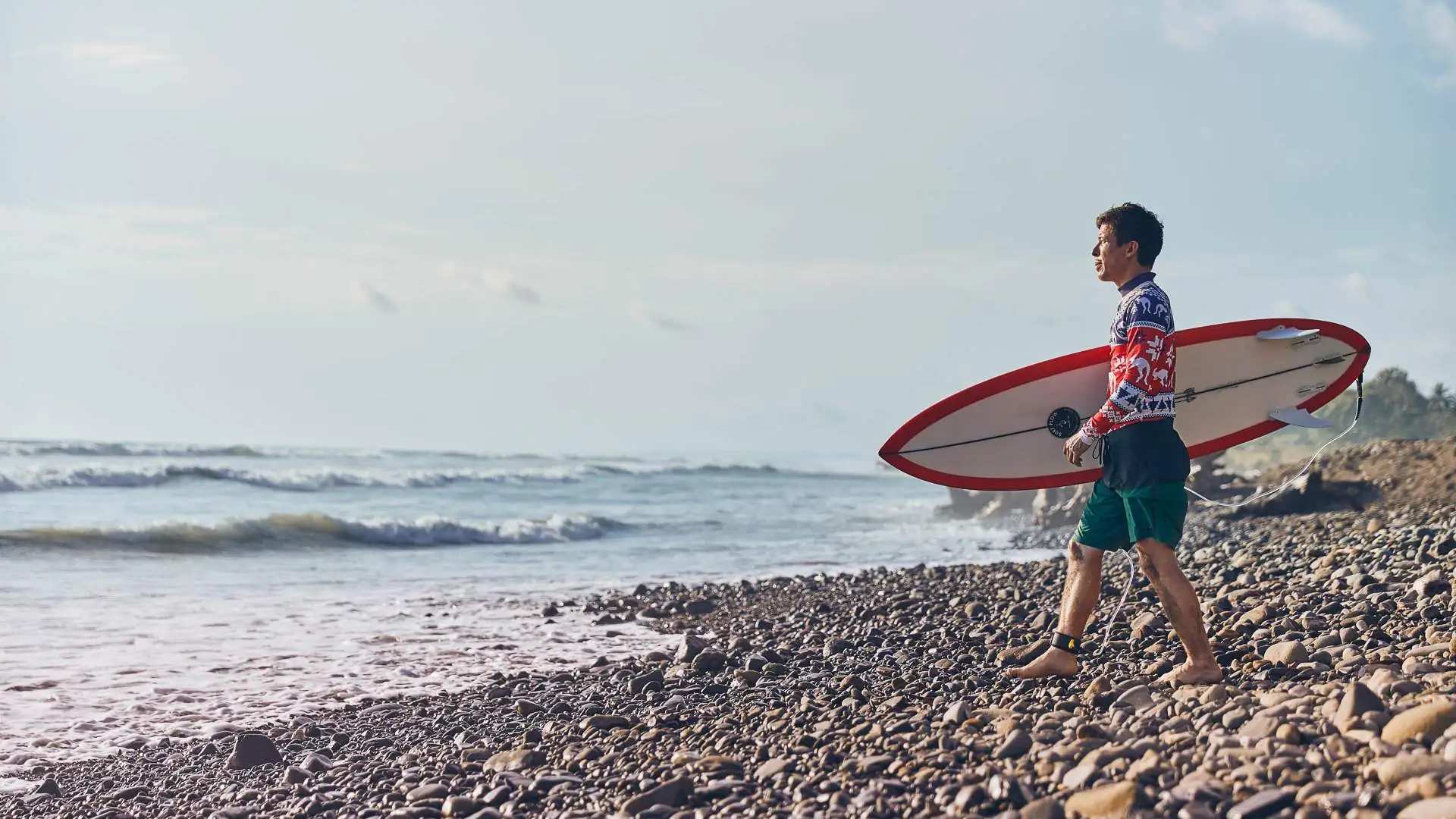 An image of a surfer stood at the beach holding a board