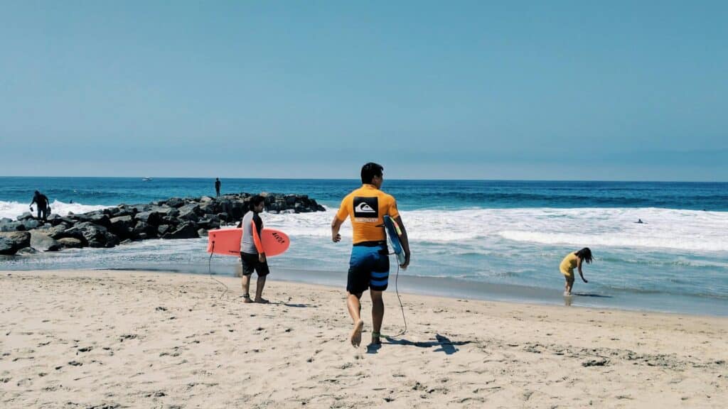 An image of a surfer walking into the sea holding a surfboard he is wearing a quicksilver top