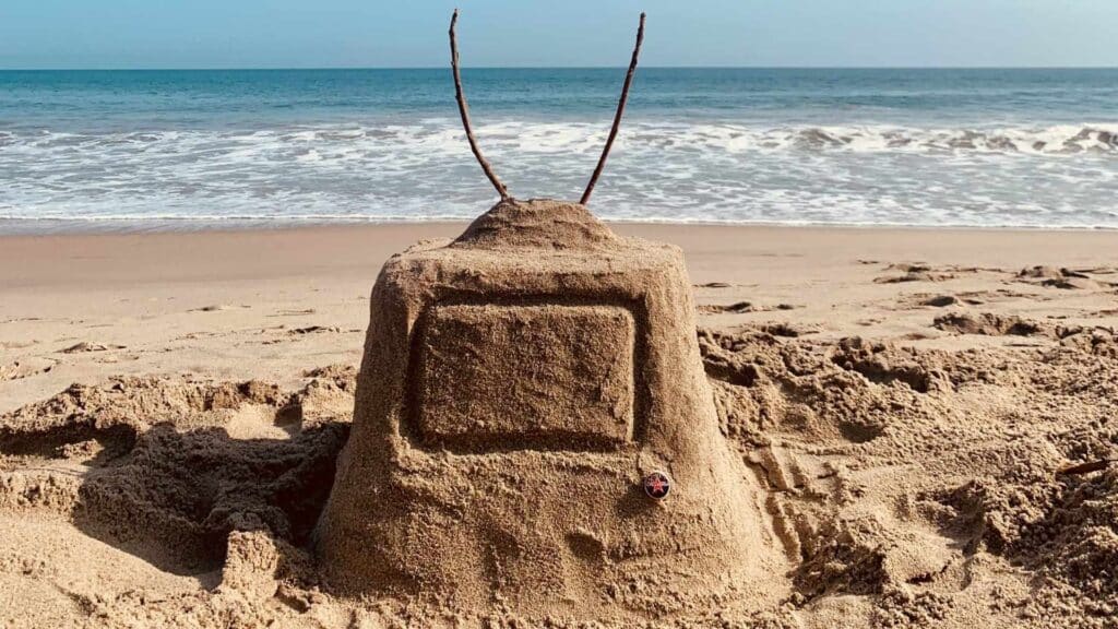 An image of a tv made of sand on the beach with the ocean in the background