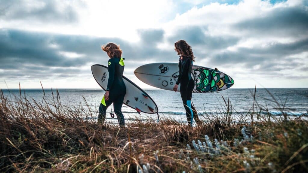 An image of two female surfers holding surf boards over looking the coast of Portugal