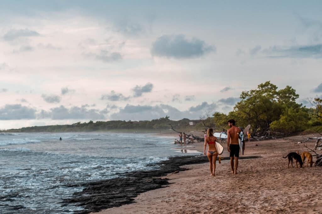 Two people with surfboards in hand walk along the shore.
