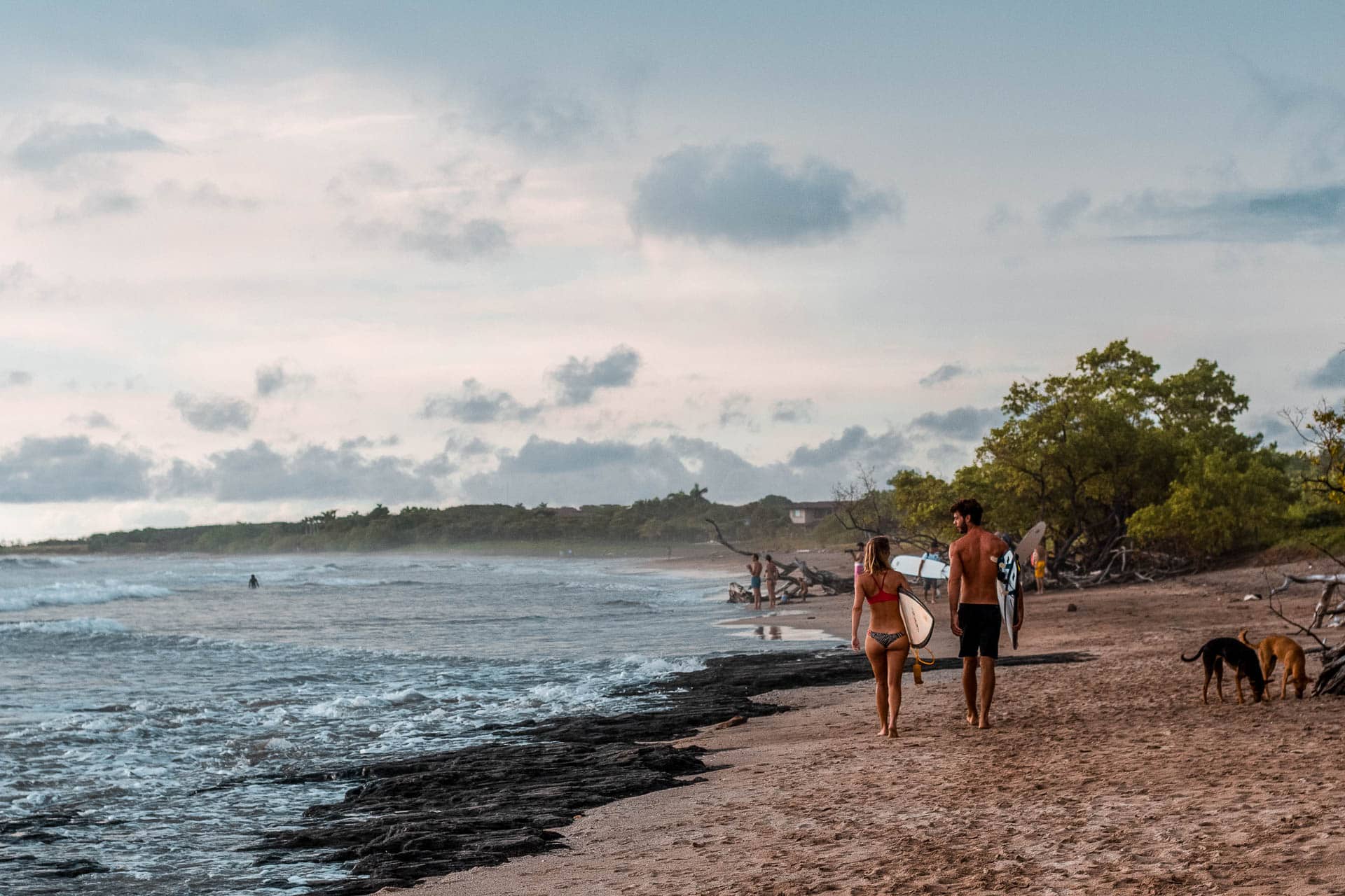 Two people with surfboards in hand walk along the shore.