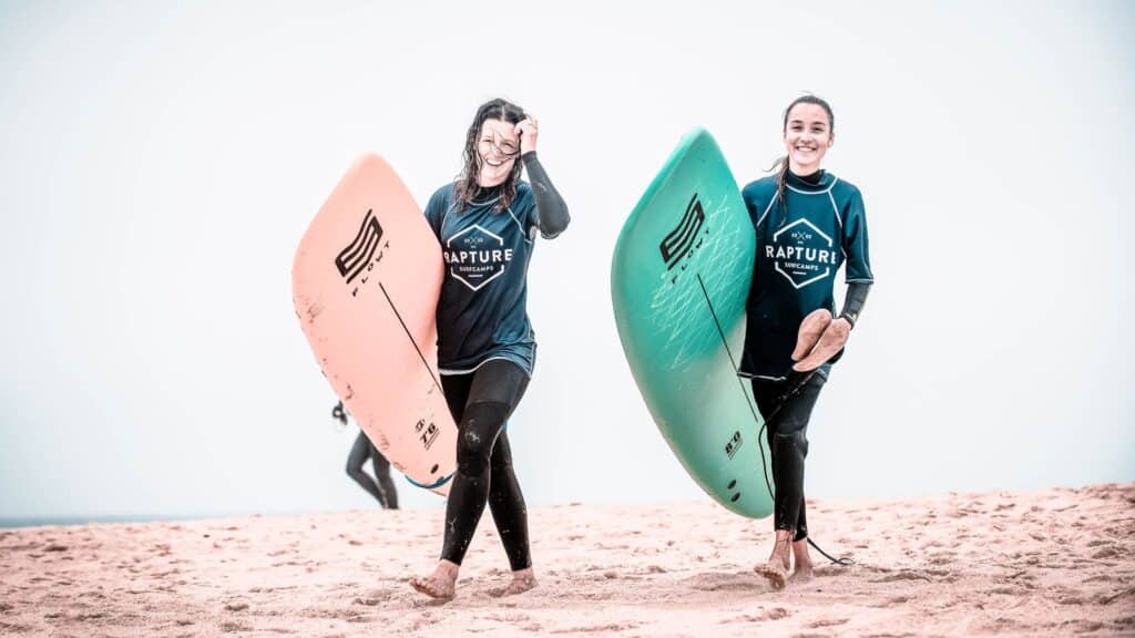 An image of two surfers at the beach in Portugal holding surfboards