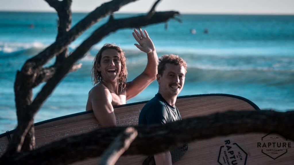 An image of two surfers smiling holding Rapture Surfcamps themed surfboards