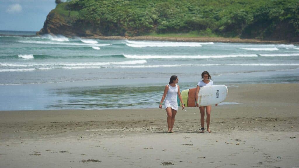 An image of two women walking on a beach in costa rica one is holding a surfboard