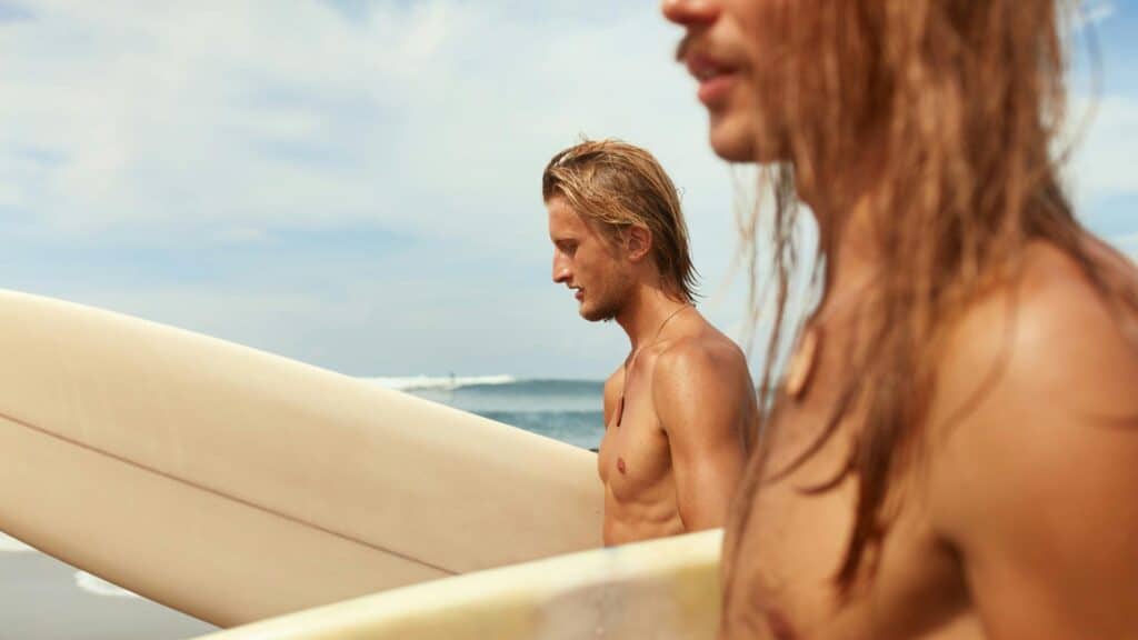 An image of two surfers with long blonde hair holding surfboards