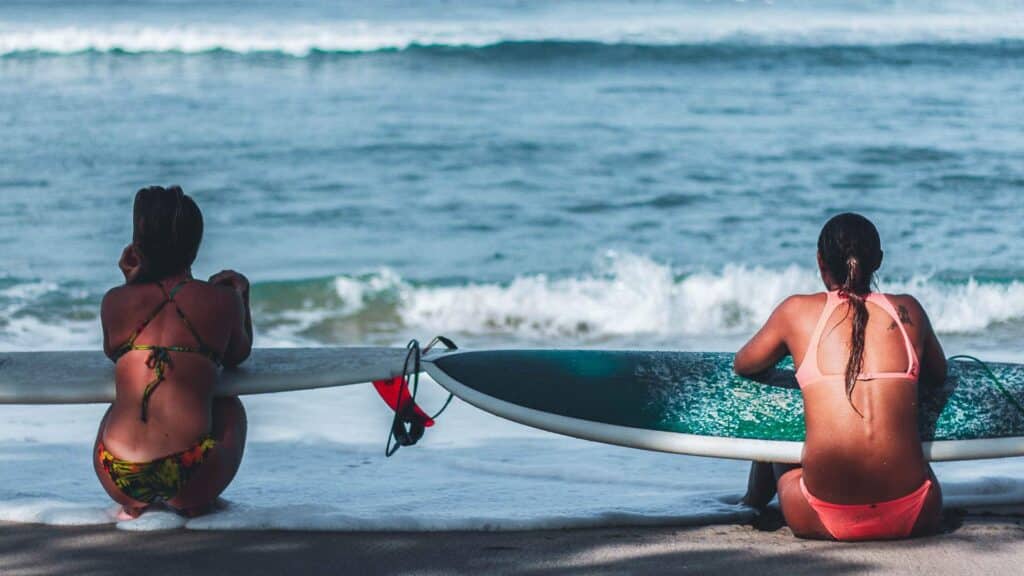 An image of two woman sat on the beach in costa rica holding surfboards