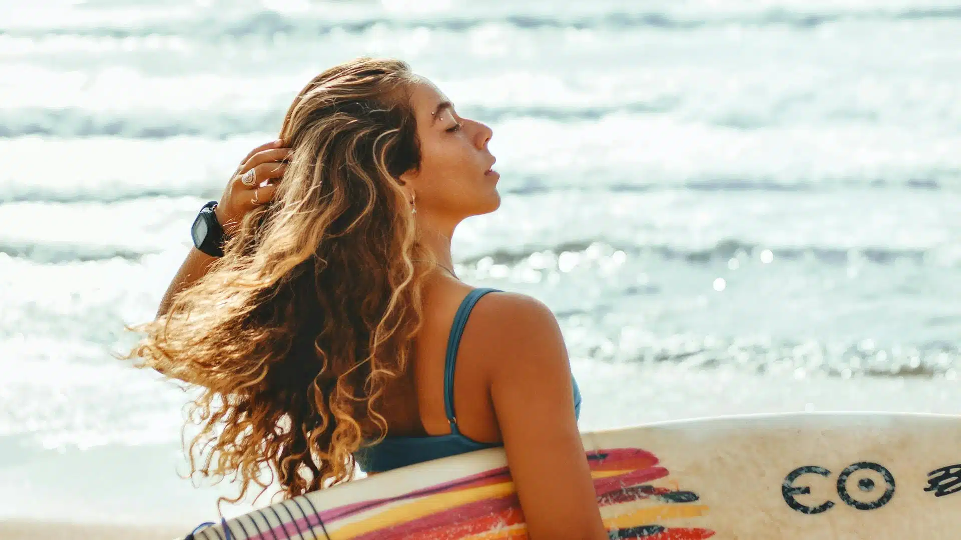 A woman on a solo trip to portugal with wavy hair holding a surfboard